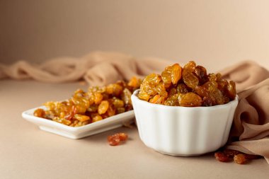 Beyaz bir kasede bej arka planda sarı sultana üzümleri. Boşluğu kopyala.