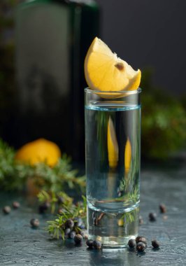 Eski koyu mavi bir masada mavi cin ve ardıç dalları. Ardıç meyveli cin, limon dilimleri ve klasik şişe..