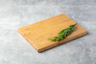 Taş bir masanın üzerinde kesme tahtası ve biberiye. Mutfak geçmişi. Boş tahta kesme tahtası, ürün görüntüleme alanı.