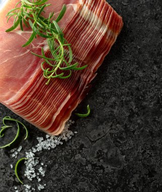 Taş bir masada dilimlenmiş prosciutto ve biberiye. Üst görünüm.