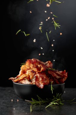 Siyah bir tabakta kızarmış pastırma, biberiye ve pembe tuz serpiştirilmiş, siyah arka planda fotokopi alanı.