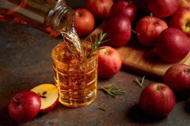 Elma suyu şişeden bardağa dökülür. Bir bardak meyve suyu ve taze elma eski bir mutfak masasında oturuyor..