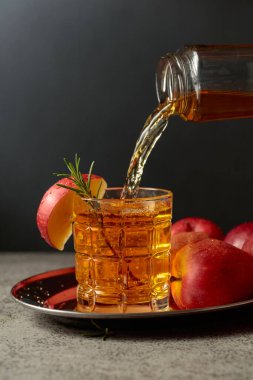 Elma suyu şişeden bardağa dökülür. Eski bir mutfak masasında elmalı taze içecek. Boşluğu kopyala.