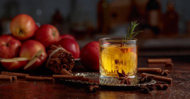 Elma dilimli elma şarabı ve biberiye filizi. Taze elmalar, tarçın çubukları ve anason eski bir mutfak masasına saçılmış..