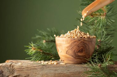 Çam fıstıkları ahşap bir kaseye dökülür. Soyulmuş çam fıstığı ve sedir dalı eski bir ahşap masada. Boşluğu kopyala.