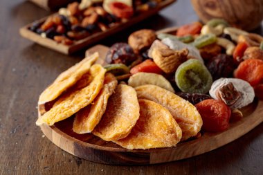 Kurutulmuş mango dilimleri, tropikal meyveler, fındıklar ve kuru üzümler eski ahşap bir masada..