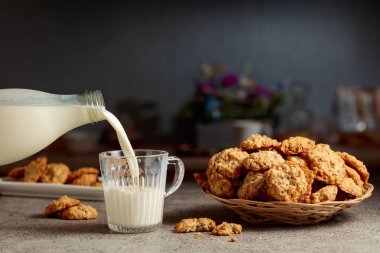 Mutfak masasında yulaflı kurabiye ve süt. Süt şişeden cam bardağa dökülür. Boşluğu kopyala.