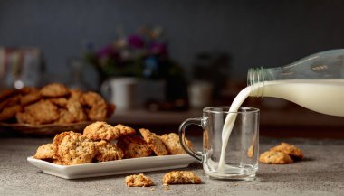 Mutfak masasında yulaflı kurabiye ve süt. Süt şişeden cam bardağa dökülür. Boşluğu kopyala.