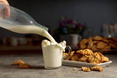 Mutfak masasında yulaflı kurabiye ve süt. Süt şişeden cam bardağa dökülür. Boşluğu kopyala.