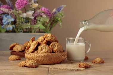 Yulaf ezmeli kurabiye ve süt, mutfak masasında dinleniyor. Süt şişeden cam bardağa dökülür. Kopyalama alanı olan bej arkaplan.