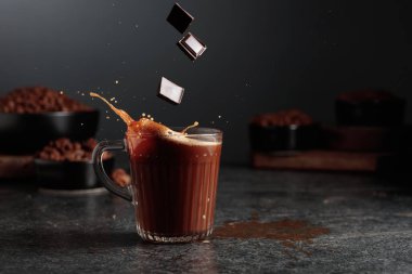 Siyah mutfak masasının üzerinde malzemeler olan bir bardak sıcak çikolata. Kakao parçacıkları bir bardak kakao içeceğinin içine düşer ve güzel bir su sıçratır..