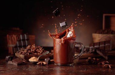 Kahverengi arka planda malzemeleri olan bir bardak sıcak çikolata. Kakao parçacıkları bir bardak kakao içeceğinin içine düşer ve güzel bir su sıçratır..