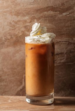 Krem şantili ve karamel soslu buzlu karamel latte, bej seramik masada ferahlatıcı ve tatlı bir kahve..