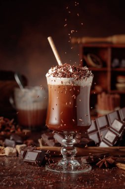 Üzerine krem şanti ve çikolata parçacıkları serpiştirilmiş sıcak çikolata. Eskimiş kahverengi arka planda yer alan malzemeler içeren bir çikolata içeceği..