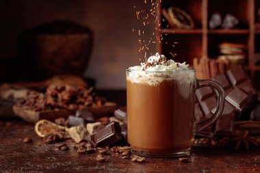 Üzerine krem şanti ve çikolata parçacıkları serpiştirilmiş çikolata içeceği. Eskimiş kahverengi arka planda yer alan malzemeler içeren bir çikolata içeceği..