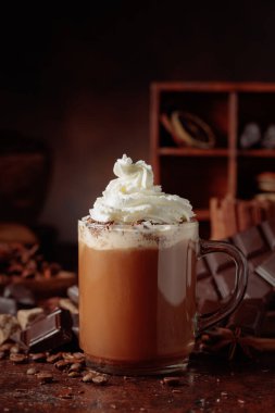 Cam bardakta krem şantili sıcak çikolata. Kahverengi arka planda malzemeleri olan çikolata içeceği..