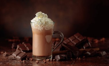 Krem şantili sıcak çikolata içeceği. Cam bardakta kakao ve koyu kahverengi arka planda acı çikolata..