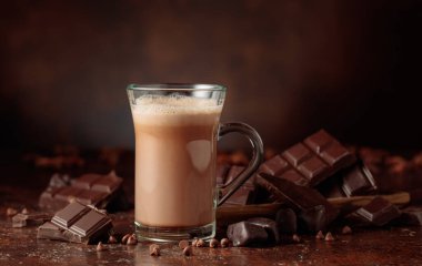 Cam bardakta sıcak çikolata ve acı çikolata parçaları. Koyu kahverengi arka plan. Alçakgönüllülük. Boşluğu kopyala.