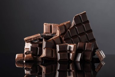 Siyah yansıtıcı arka planda kırık acı ve sütlü çikolatalar. Boşluğu kopyala.