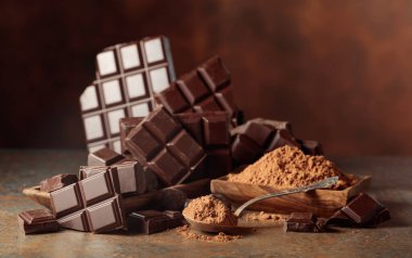 Kırık çikolata ve kahverengi arka planda kakao tozu. Boşluğu kopyala.