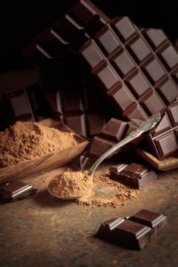 Kırık çikolata ve kahverengi paslı arka planda kakao tozu..