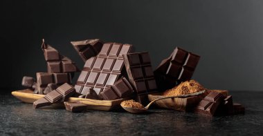 Siyah arka planda kırılmış siyah çikolata ve kakao tozu. Boşluğu kopyala.