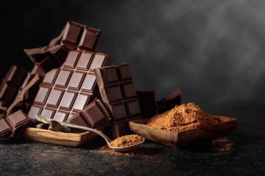 Siyah arka planda kırılmış siyah çikolata ve kakao tozu. Boşluğu kopyala.