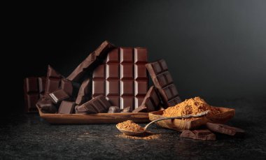 Siyah arka planda kırılmış siyah çikolata ve kakao tozu. Boşluğu kopyala.