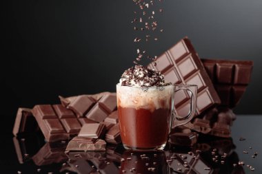 Krem şantili ve çikolata kırıntısı serpiştirilmiş sıcak çikolata. Arka planda kırık bir çikolata parçasında. Siyah yansıtıcı arkaplan.