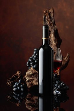 Şişe ve bir bardak kırmızı şarap. Arka planda eski yıpranmış çıkıntı ve mavi üzümler. Boşluğu kopyala.