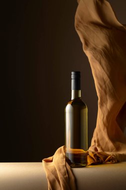 Bir şişe beyaz şarap ve koyu bir arkaplanda bej rengi kumaş..