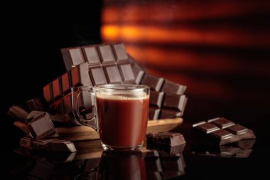 Bir kupa sıcak çikolataya karşı kırık çikolatalar. Siyah parlak arka plan derinlik ve yansıma ekler. Boşluğu kopyala.