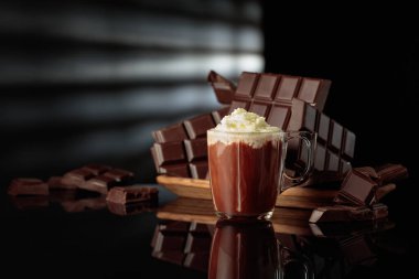 Kırık çikolatalara karşı krem şantili sıcak çikolata. Siyah parlak arka plan derinlik ve yansıma ekler. Boşluğu kopyala.