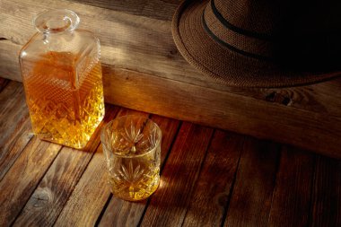 Zarif viski bardağı ve kehribar sıvısıyla dolu sürahi eski bir ahşap masada. Boşluğu kopyala.