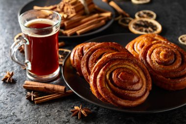 Kanelbullar - İsveç tarçınlı çörekler ya da dürümler. Siyah taş bir masada taze pişmiş çörekler..