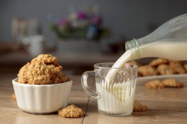 Mutfak masasında yulaflı kurabiye ve süt. Süt şişeden cam bardağa dökülür. Boşluğu kopyala.