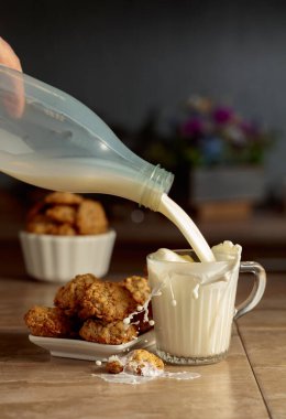 Mutfak masasında yulaflı kurabiye ve süt. Süt şişeden cam bardağa dökülür. Boşluğu kopyala.