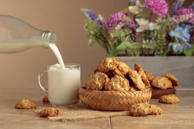 Yulaf ezmeli kurabiye ve süt, mutfak masasında dinleniyor. Süt şişeden cam bardağa dökülür. Kopyalama alanı olan bej arkaplan.