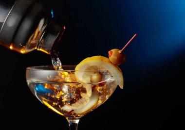 Yeşil zeytinli ve limonlu martini. Kokteyl bardaktan bardağa dökülüyor..