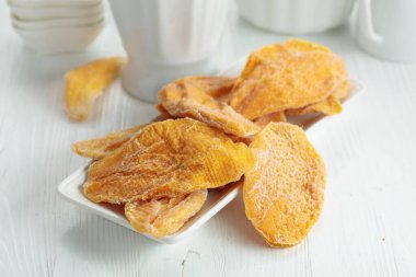 Beyaz ahşap bir masada kurutulmuş mango dilimleri..