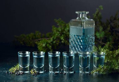 Mavi cin ve ardıç dalları eski, koyu mavi bir masada. Ardıç meyveli cin. Boşluğu kopyala.
