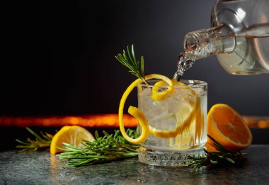 Limon ve biberiyeli cin tonik kokteyli. İçki şişeden buzlu bir bardağa dökülür. Boşluğu kopyala.