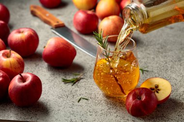 Elma suyu şişeden bardağa dökülür. Bir bardak meyve suyu ve taze elma eski bir mutfak masasında oturuyor..