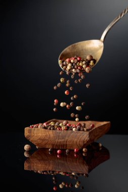 Siyah arka planda karabiber karışımı. Siyah, kırmızı, beyaz ve baharatlı biberler ahşap tabağa dökülür..