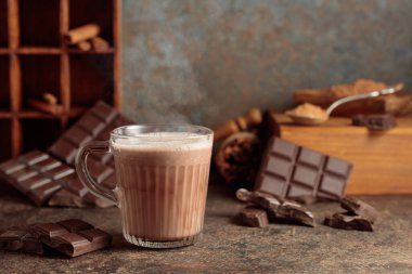Kahverengi arka planda sıcak çikolata içeceği. Bir kupa sıcak çikolata, kırık çikolata ve kakao tozu. Boşluğu kopyala.