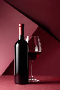 Kırmızı arka planda bir şişe kırmızı şarap. Boşluğu kopyala.
