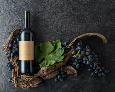 Bir şişe kırmızı şarap, mavi üzüm ve siyah taşlı arka planda eski asma parçaları. Üst Manzara. Boşluğu kopyala.