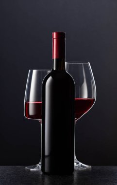 Siyah arka planda kırmızı şarap şişesi ve bardakları..