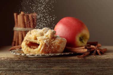 Eski ahşap masada elma ve tarçınlı Viyana turtası. Üzerine pudra şekeri serpilmiş taze pişmiş yiyecekler..