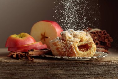 Eski ahşap masada elma ve tarçınlı Viyana turtası. Üzerine pudra şekeri serpilmiş taze pişmiş yiyecekler..